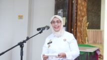 a woman in a white coat holding a piece of paper in front of a microphone